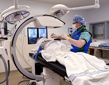 Wallace Ralston, DNP, CRNA performs a pain procedure on a patient in a CCMH operating room.Photo of patient lying on table in operating room undergoing a pain procedure by a CRNA using radiologic guided assistance.